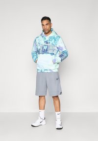 Hanorac cu glugă în nuanțe de albastru deschis și mov, combinat cu pantaloni scurți atletici gri. Modelul poartă teniși albi și șosete.