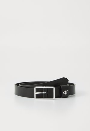 Cintura in pelle nera con fibbia rettangolare argentata e un piccolo logo "cK" argentato sul cinturino, avvolta su uno sfondo bianco.