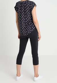 Marinblus med blommönster och korta volangärmar, matchad med svarta kortbyxor och vita sneakers. Slät tyg, avslappnad passform och ryggdetalj synlig.