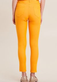 Geel denim skinny jeans met een hoge taille, twee achterzakken en gestikte details, gecombineerd met lichtgekleurde, platte schoenen.