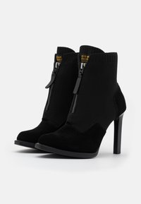 Botas de tobillo negras con tacón alto, con material de ante y parte superior de punto, cierre de cremallera y un diseño distintivo.