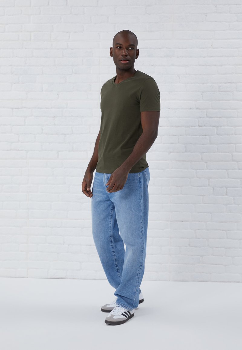 Mørkegrøn v-neck t-shirt, blå denim jeans og sort-hvide sneakers. Slim fit, glat tekstur og afslappet design.