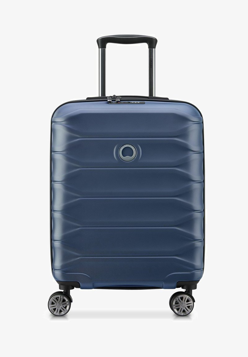 Valigia rigida blu con superficie testurizzata, righe orizzontali, manico retrattile e quattro ruote girevoli per la mobilità.