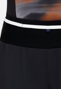 Svarta atletiska shorts med en texturerad svart midja och en vit accentrand. Tyget verkar lätt och andningsbart.