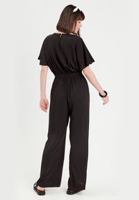 Schwarzer Jumpsuit mit kurzen, flatternden Ärmeln und elastischem Bund. Mit einem Schlüsselloch-Rücken und weiter Beinform. Aus glattem, leichtem Stoff.
