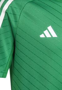 Maglia sportiva verde in tessuto testurizzato, con strisce diagonali bianche e logo Adidas sul lato sinistro superiore.