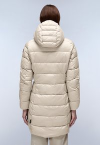 Abrigo acolchado de color beige claro con capucha ajustada, diseño acolchado, longitud hasta el muslo y detalle de logotipo sutil en el dobladillo. Textura suave y brillante.