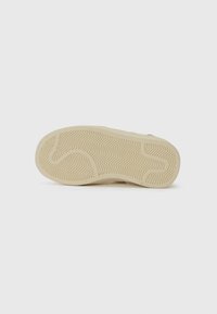 Sula av sko med beige gummimönster som har zickzack- och kurviga linjer på en vit bakgrund.