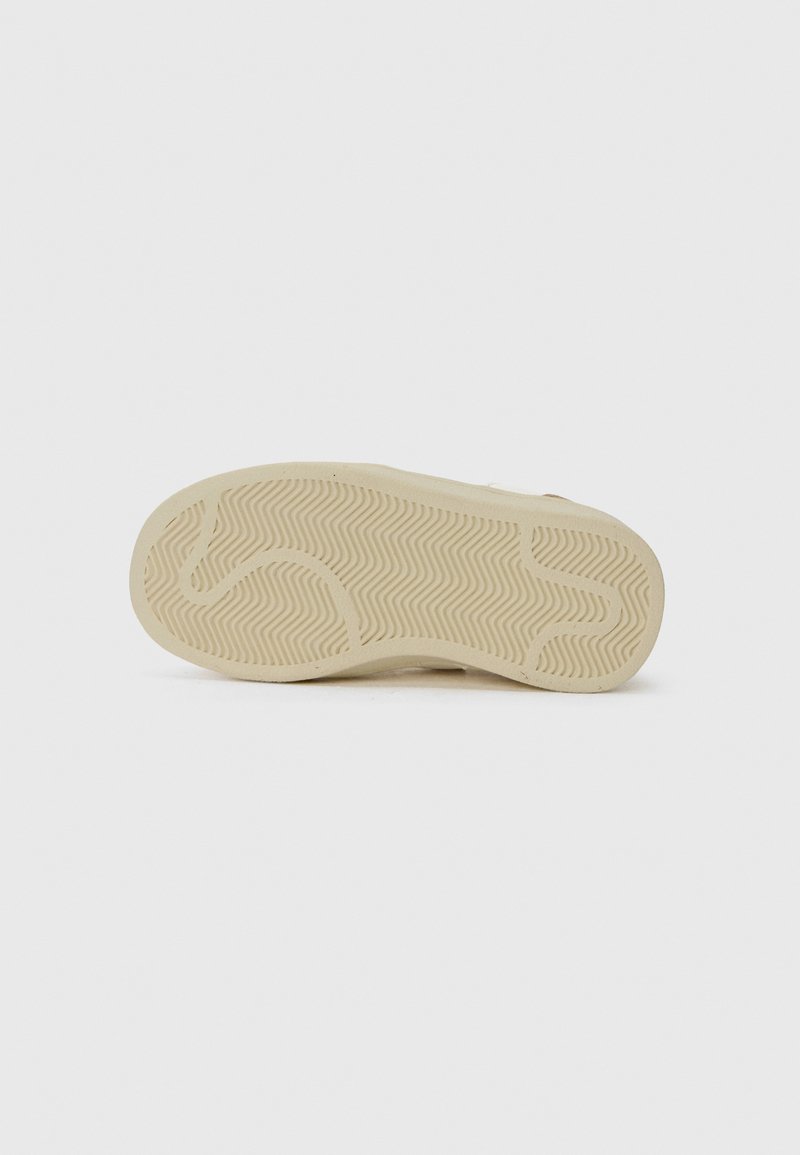 Suola della scarpa con un motivo in gomma beige che presenta linee zigzag e curve su uno sfondo bianco.