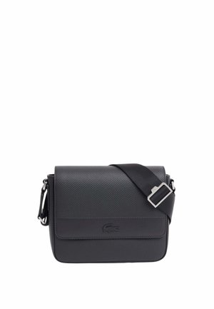 Bolso cruzado negro con textura, correa ajustable y logotipo de cocodrilo en relieve en la solapa frontal.