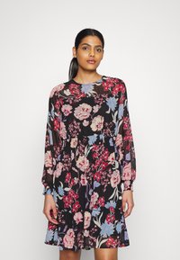 Vestido preto com padrão floral, incluindo mangas longas, gola redonda e bainha em camadas. O padrão apresenta flores vermelhas e azuis em um tecido transparente.