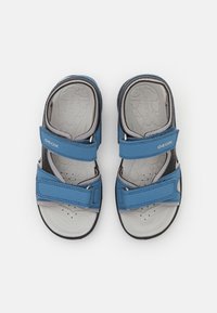 Sandalias azules de material sintético con dos correas de Velcro ajustables, plantillas grises con un patrón texturizado y suelas de goma negras.