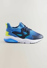 Chaussure de sport bleue avec une tige lisse en bleu marine et bleu clair, ornée d'accents verts et noirs, d'une semelle blanche rembourrée et de lacets texturés.