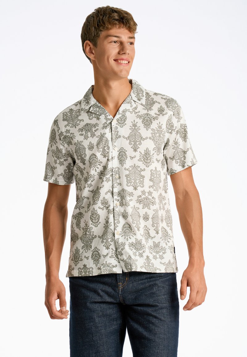 Camisa de manga corta en color beige claro con intrincados patrones florales y de paisley en verde, que cuenta con un collar tipo botón y un corte relajado.