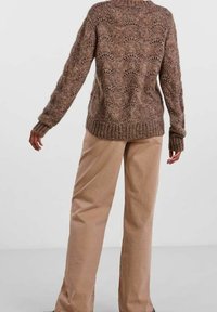 Strickpullover in Brauntönen mit einer strukturierten, gemusterten Optik; kombiniert mit hellbeigen, locker sitzenden Hosen. Material aus Wolle.