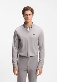 Ανοιχτό γκρι πουκάμισο με κουμπιά και μακριά μανίκια από υφασμάτινη υφή, με γιακά και μικρό μαύρο λογότυπο "BOSS" στο στήθος.