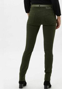 Pantalones verdes ajustados de denim con una textura suave, que cuentan con bolsillos traseros y un patrón sutil en la cinturilla.