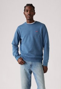 Blauwe sweatshirt gemaakt van zacht materiaal met een ronde hals, geribbelde mouwen en onderkant, met een klein rood Levi's logo op de borst.