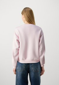 Rosa sweatshirt med rund halsringning, ribbade mudd och nederkant. Bärs med högmidjade, urtvättade blå jeans, som visar en avslappnad passform.