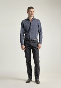 Camisa de manga larga azul marino con botones, de corte ajustado, combinada con pantalones oscuros y zapatos negros. Tela suave con una textura sutil y un detalle mínimo.