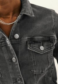 Black denim jacket featuring a collar, silver snap buttons, chest pocket, and tonal stitching, with a textured, distressed appearance.