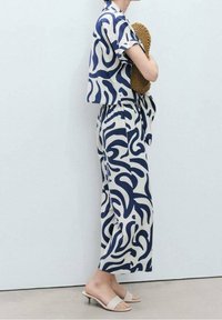 Dvoudílný outfit složený z krátkého topu s krátkými rukávy a kalhot s širokými nohavicemi v námořnickém modrém abstraktním vírovém vzoru na krémovém pozadí.