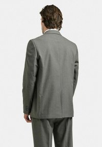 Grå kavaj med slag, en slits bak och knäppta ärmar. Tillverkad av textil med strukturerad yta och skräddarsydd passform.