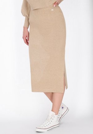 Beige pletená midi sukně s bočním rozparkem, která má jemnou strukturu. V kombinaci s bílými vysokými teniskami, což vytváří neformální styl.