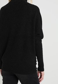 Pull noir tricoté avec une coupe ample et un col montant. Le tissu semble texturé avec une sensation douce et chaude, et des manches longues.