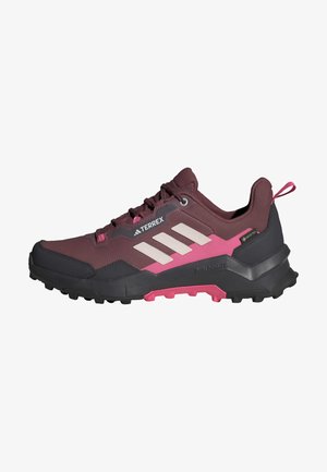 Trailrunning-Schuhe mit einem burgunderfarbenen Obermaterial, pinken Akzenten und einer schwarzen Gummisohle mit strukturiertem Grip; enthält weiße Markenstreifen.