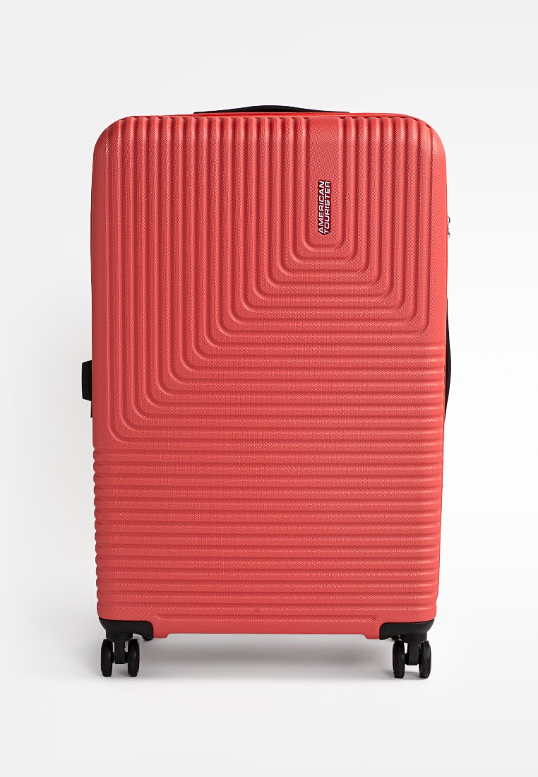 Valise rigide de couleur corail avec un design texturé à rayures. Dotée d'une poignée et de quatre roues pour plus de mobilité. Logo de la marque affiché.