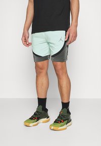Ljus mynta gröna träningsshorts med svarta och vita randiga detaljer, parat med svarta och olivgröna sneakers med orangea detaljer.