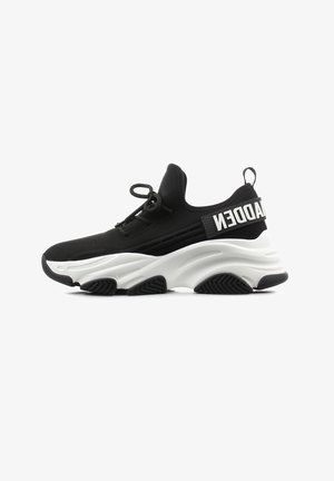 Scarpa sportiva nera con tomaia testurizzata, suola intermedia bianca e suola esterna in gomma nera. Caratterizzata da lacci elastici e un’etichetta sul tallone con logo.