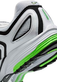 Scarpa sportiva bianca con dettagli neri e verdi, dotata di tomaia in mesh testurizzato, colletto imbottito e suola dettagliata.
