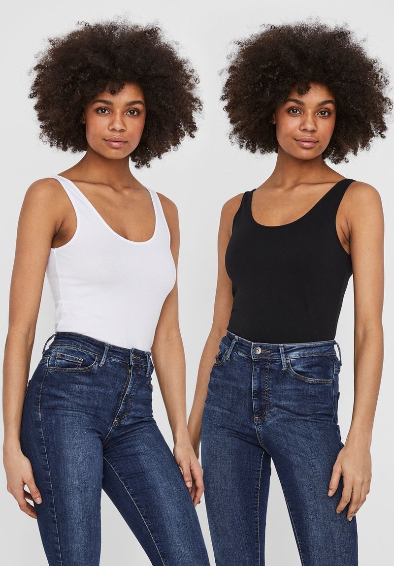 Deux femmes portant des débardeurs ajustés, l'une en blanc et l'autre en noir, accompagnés de jeans en denim bleu taille haute, mettant en valeur des textures et des contours lisses.