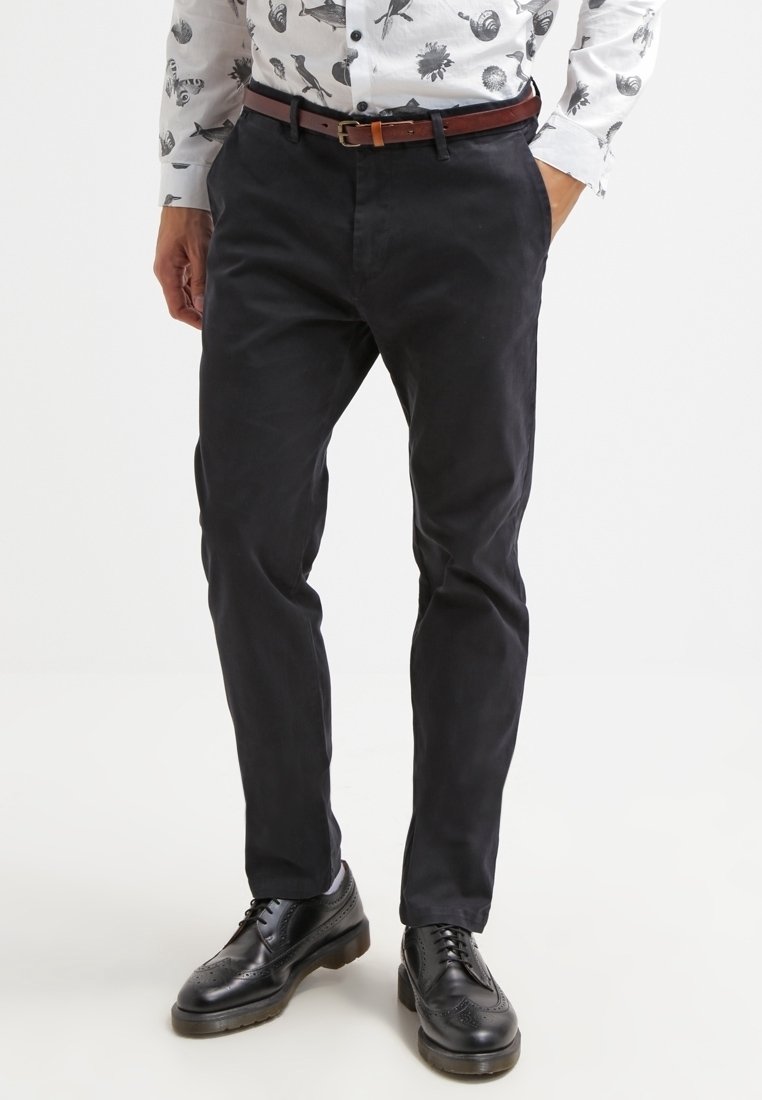 Dark blue chinos with a slim fit, made of cotton blend fabric, featuring front pockets and a belt. Paired with black leather shoes.