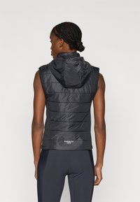 Veste sans manches matelassée noire avec capuche, texture matelassée, fermeture éclair frontale et logo sur l'ourlet. Matière lisse et légère.