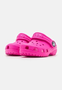 Jasně růžové clogs značky Crocs vyrobené z lehkého syntetického materiálu, s ventilačními otvory, vyvýšenou texturovanou podrážkou a nastavovací patní sponou.