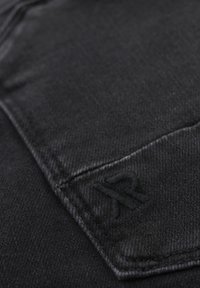 Czarna dżinsu tkanina o gładkiej fakturze. Ma przyszytą kieszeń i subtelnie wyszywane logo. Ogólnie monochromatyczny wzór.