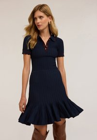 Robe polo en tricot marine à manches courtes, texture côtelée, bords festonnés, patte de boutonnage et jupe évasée.
