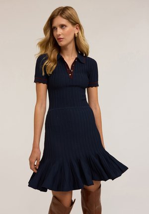 Knit polo dress in navy with short sleeves, ribbed texture, scalloped edges, button placket, and a flared skirt.
