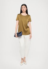 Olive green short-sleeve top, lightweight fabric, relaxed fit. Paired with white wide-leg trousers and a textured navy clutch bag.