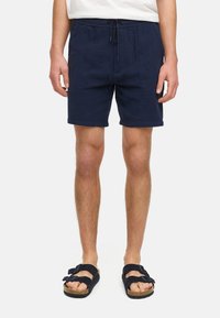 Navykleurige shorts van een textuurstof, met een elastische tailleband en een trekkoord, en getoond met zwarte sandalen.