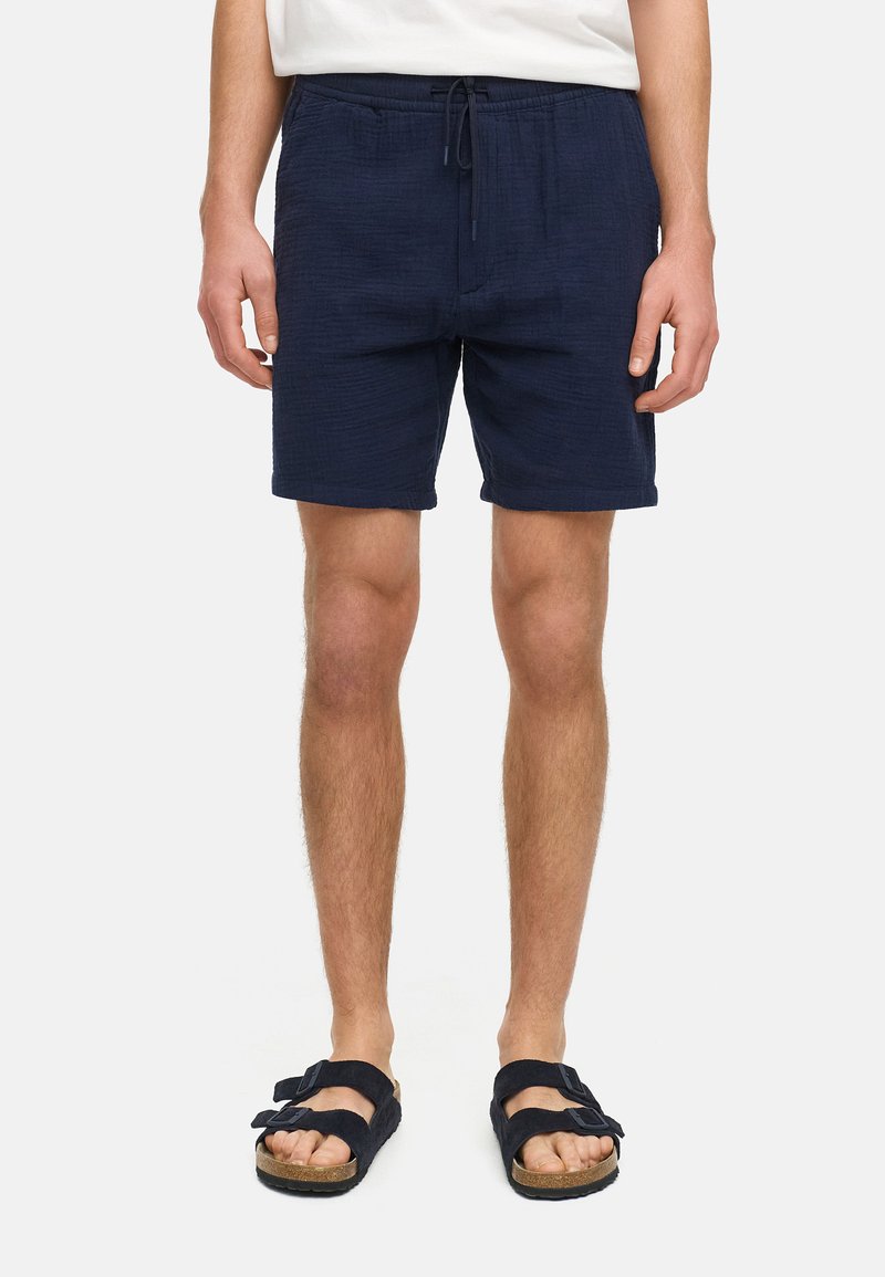Navykleurige shorts van een textuurstof, met een elastische tailleband en een trekkoord, en getoond met zwarte sandalen.
