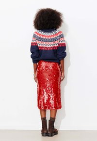 Pull en maille bleu marine avec motif flocon de neige rouge et blanc, associé à une jupe crayon rouge brillante à sequins et des bottines marron.