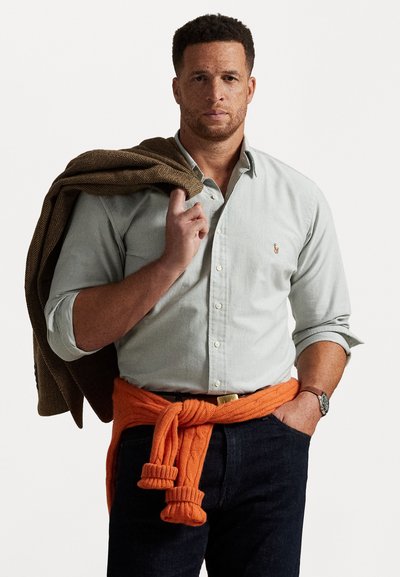 Šviesiai žalia mygtukinė marškinėliai, tamsiai mėlyni džinsai, oranžinė megzta liemenė surišta ties liemeniu, ruda zigzaginė striukė užmesta ant peties.