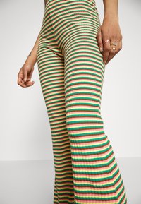 Gestreepte uitlopende broek met groen, rood, roze en gele kleuren. Het materiaal lijkt ribbelig, wat de levendige patronen langs de benen benadrukt.