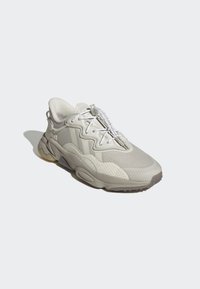 Sneaker beige clair avec une tige texturée, un design superposé, des lacets réglables et une semelle épaisse dotée d'un motif de traction.