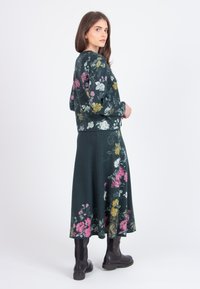 Knit floral dress and sweater set in dark green with pink, yellow, and white flower patterns; paired with black knee-high boots.