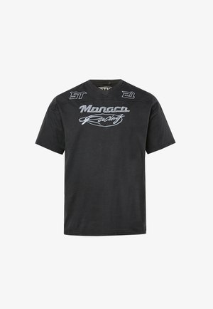Schwarzes kurzärmeliges T-Shirt mit der Stickerei "Monaco Racing" auf der Vorderseite sowie den Aufnähern "21" und "ST" in der Nähe des Halsausschnitts.